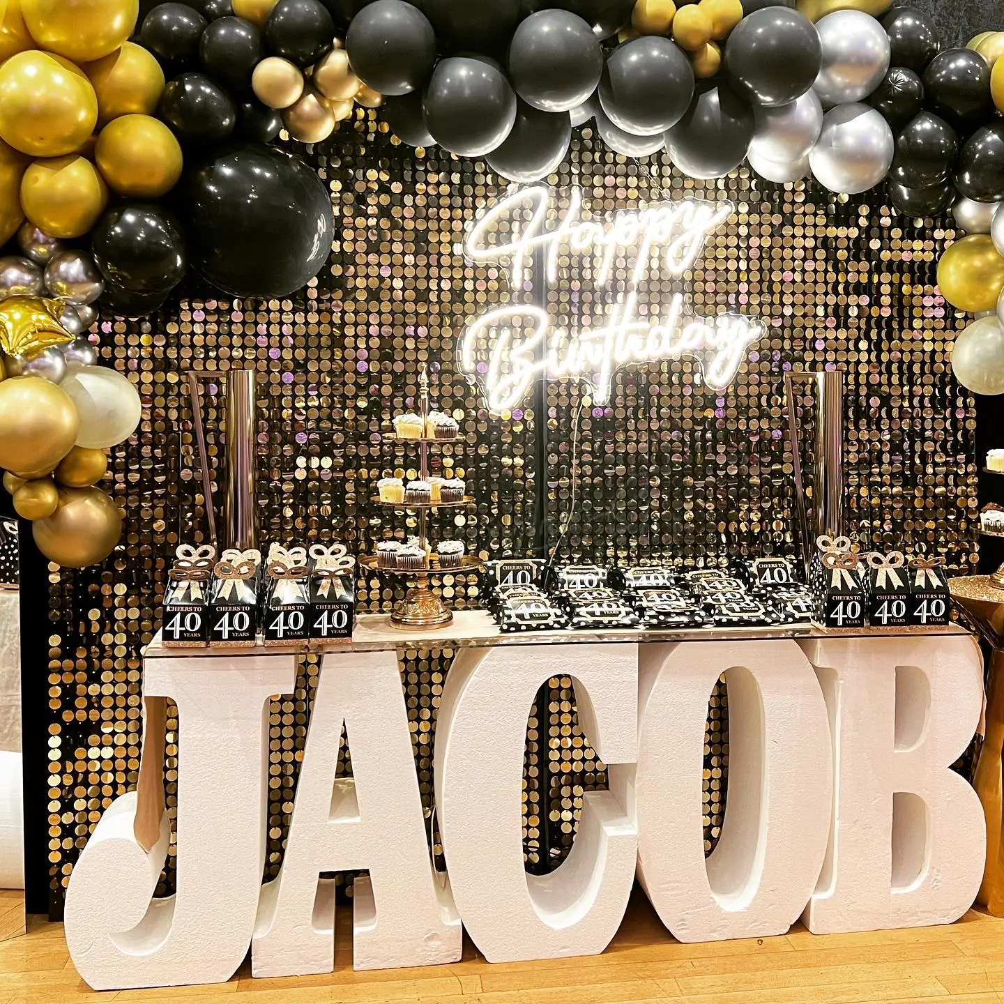 Black and gold birthday display with balloons, desserts, and marquee letters