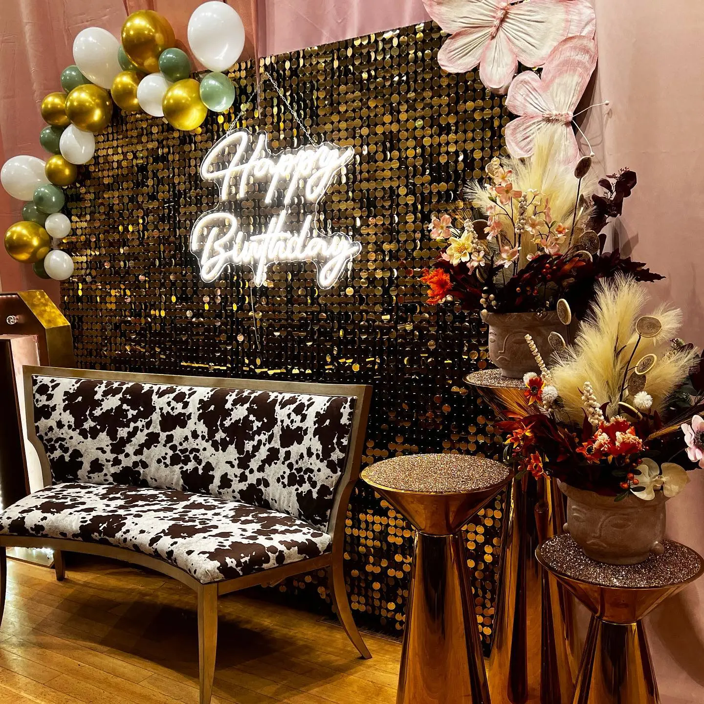 Birthday photo backdrop with gold sequins, balloons, flowers, and a patterned loveseat