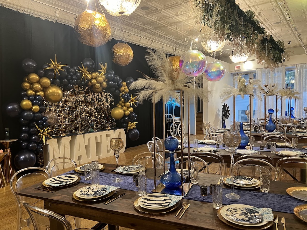 Navy and gold party setup with sequin backdrop, marquee letters, and feather centerpieces