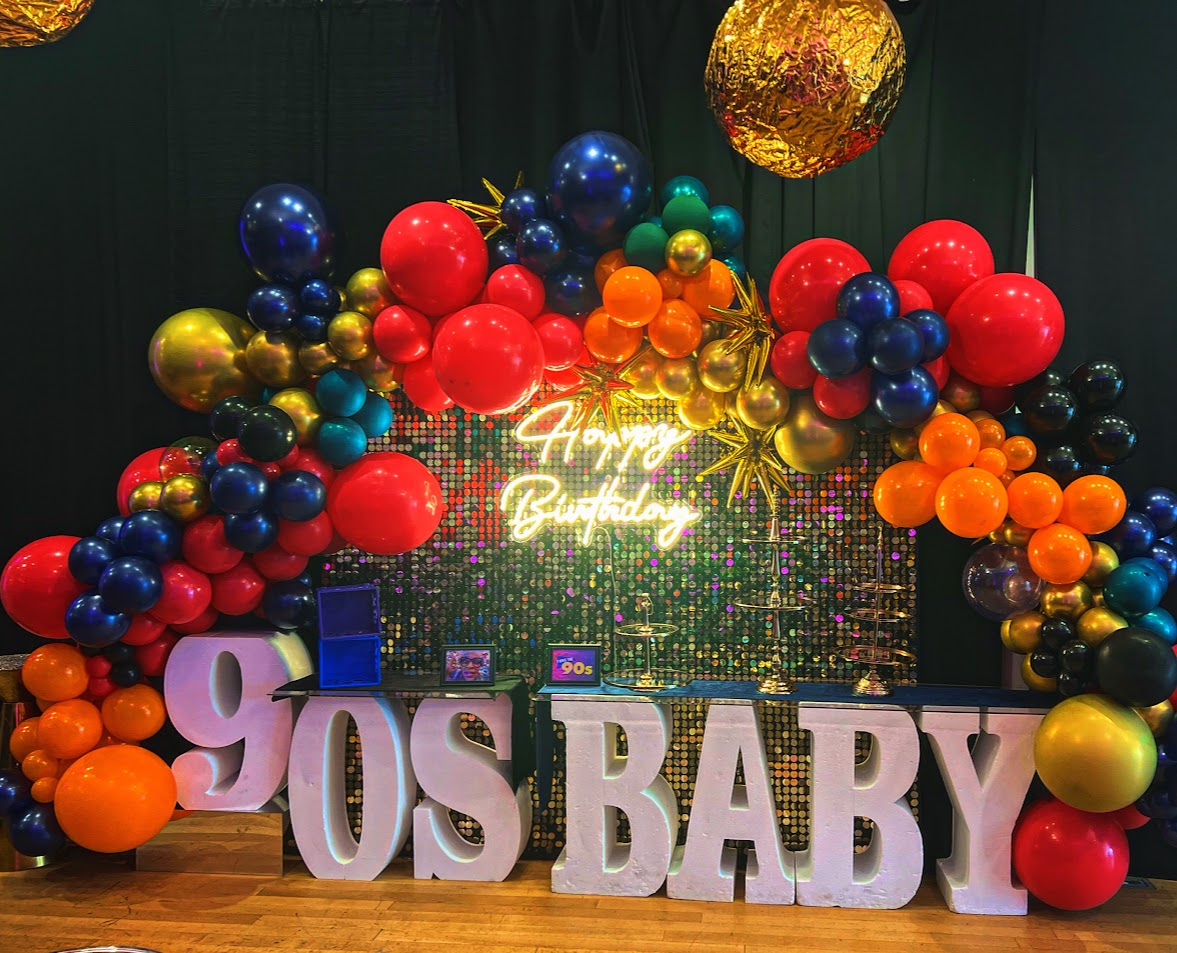 Colorful 90s themed birthday backdrop with balloon arch and neon Happy Birthday sign