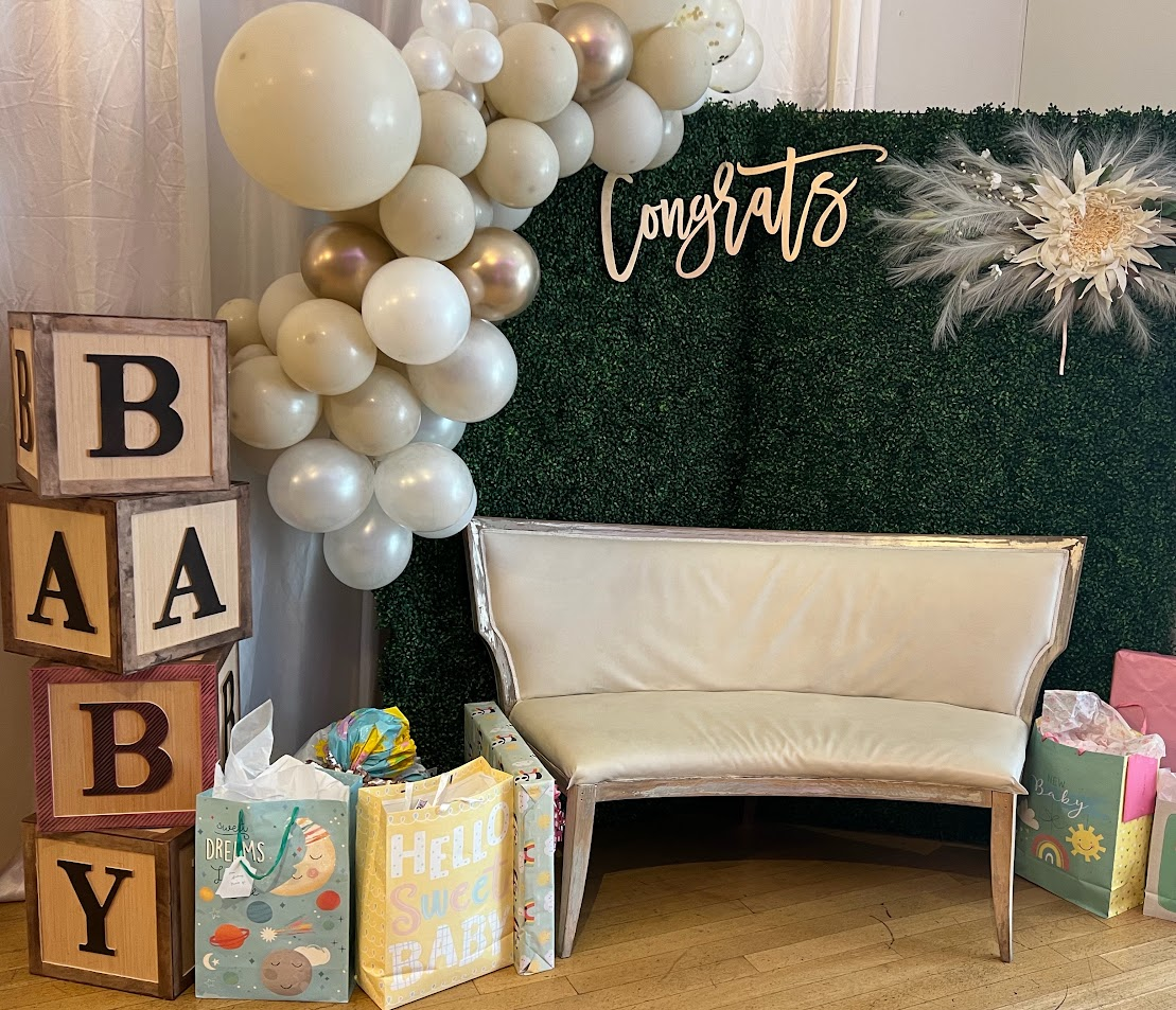 Baby shower corner with greenery wall, Congrats sign, cream settee, and BABY blocks