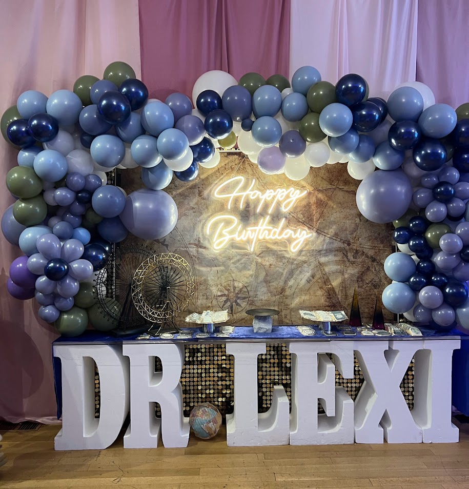 Travel themed birthday table with blue balloon arch, vintage map backdrop, and marquee name letters