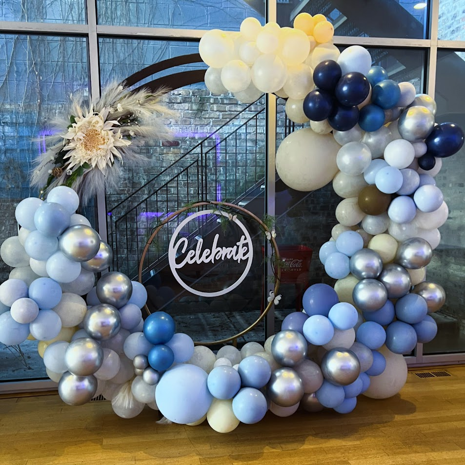 Blue and silver balloon hoop with a Celebrate sign in front of tall windows