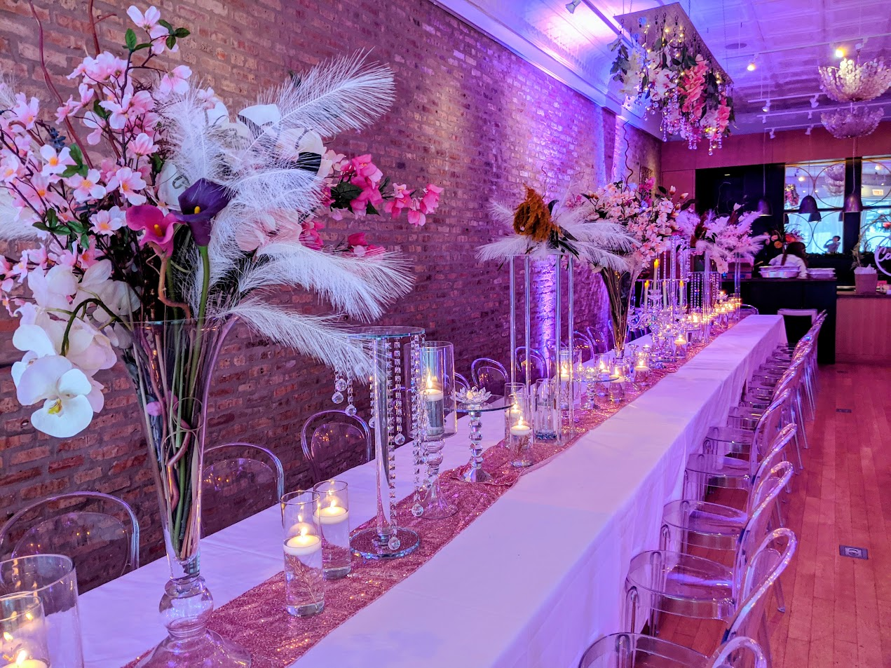 Long white head table with pink florals, feather centerpieces, candles, and clear chairs