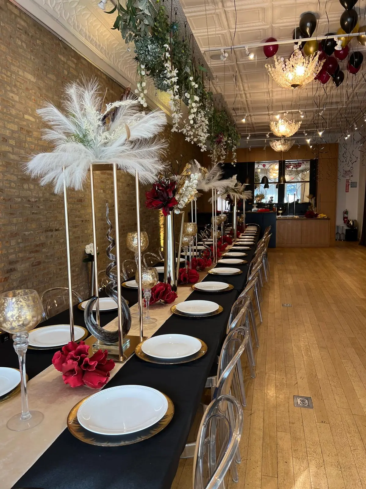Long black-linen table with gold chargers, red florals, and feather centerpieces