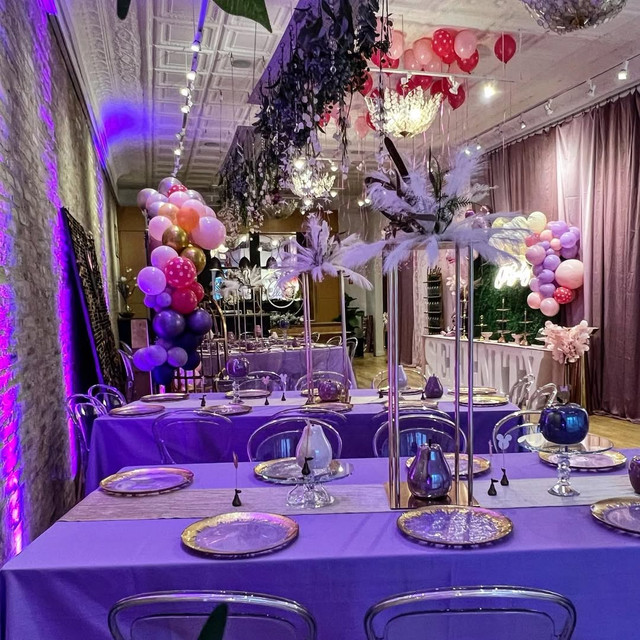 Purple birthday dinner setup with balloon arrangements and clear chairs