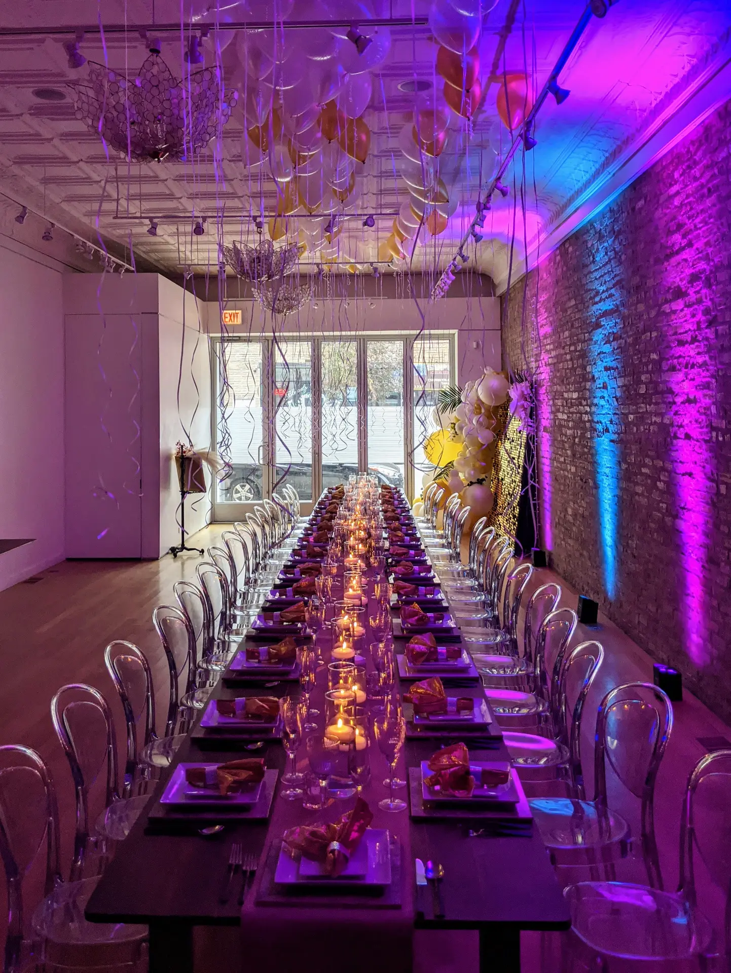 The Long Hall set for a candlelit celebration with purple uplighting, balloons, and a long banquet table